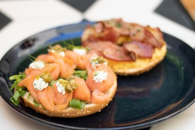 Bagel aberto, coberto, num dos lados, com salmão e crème fraîche e, no outro, com ovos e bacon